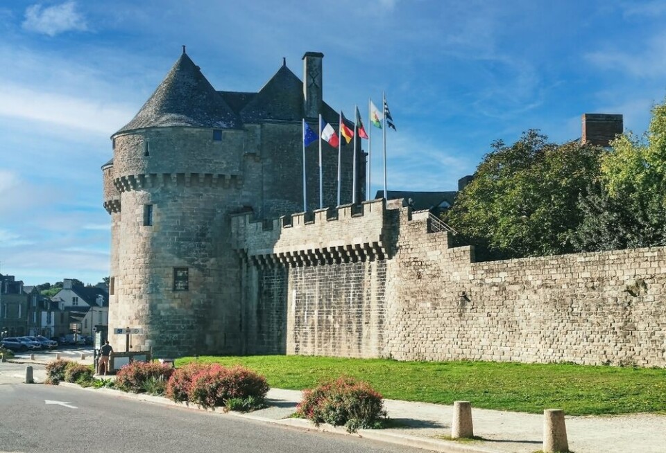 Medieval stone walls and gate tower of Guérande on a sunny day with flags flying.