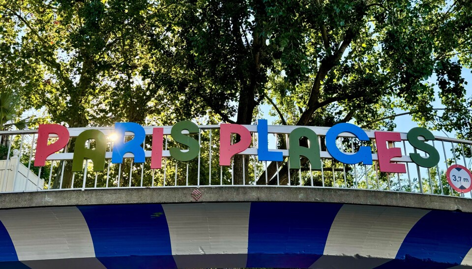 Colourful Paris Plages sign on a bridge under trees.