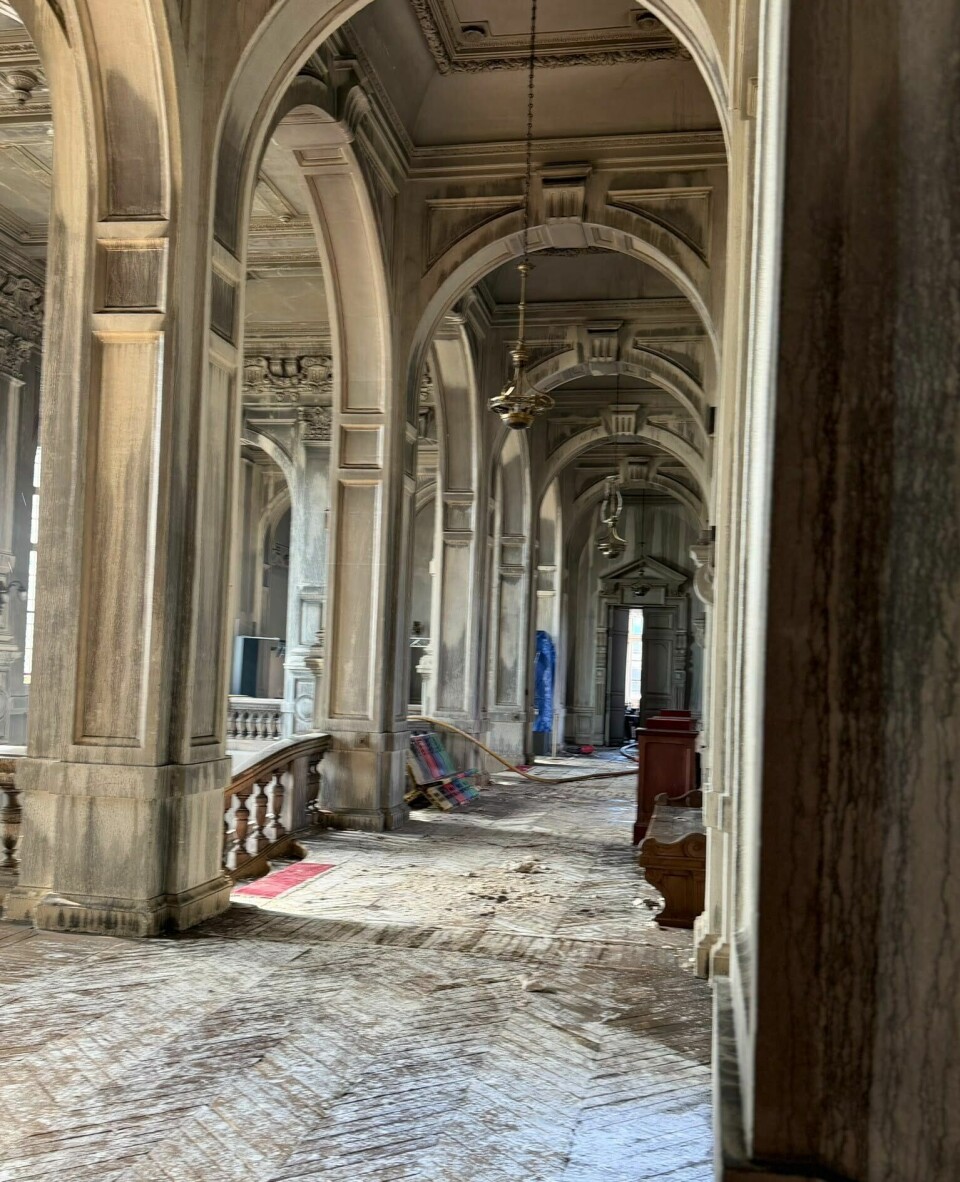 Ornate stone colonnade with arches, columns and patterned flooring leading to a distant doorway