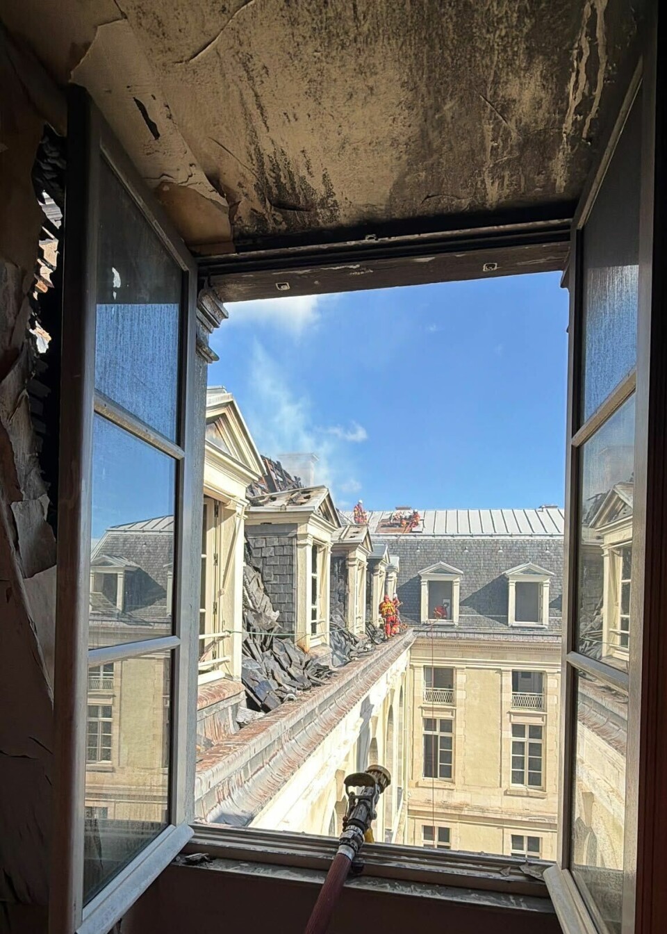Charred room framing an open window overlooking historic slate-roofed buildings