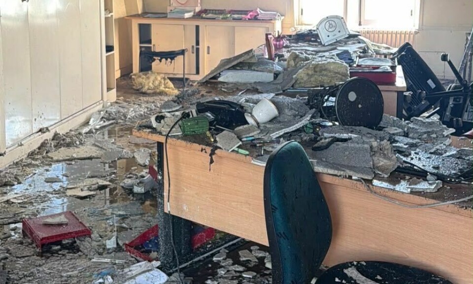 Damaged room with rubble, overturned chairs, broken desks and an exposed ceiling